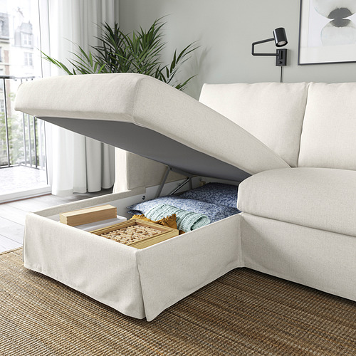 Un moderno sofá color crema con una chaise longue elevable que revela el espacio de almacenamiento que contiene mantas y juegos de mesa.