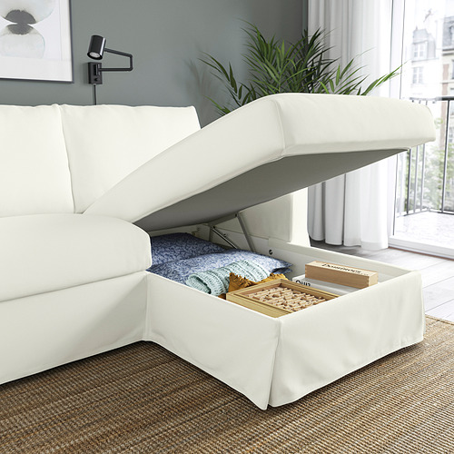 Un moderno sofá blanco con una chaise longue elevable que revela juegos de mesa y mantas en el almacenamiento.