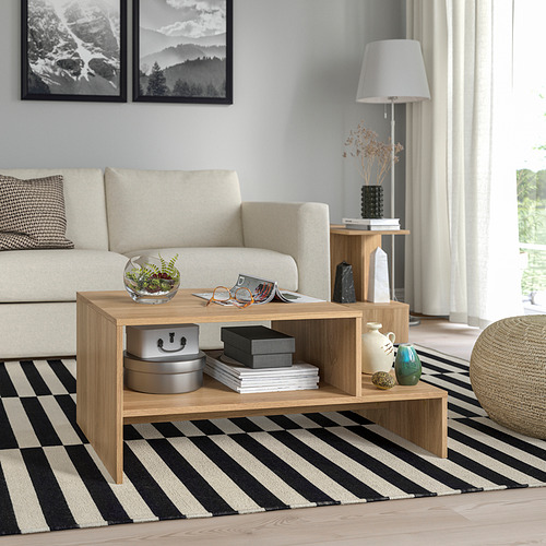 Sala de estar moderna con mesa de centro de madera clara HOLMERUD, sofá beige acolchado, alfombra de rayas blancas y negras y elementos decorativos.