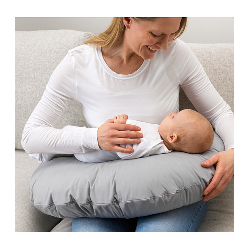 Mujer con camisa blanca se sienta en el sofá con bebé y almohada de lactancia gris.