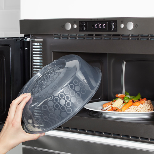 Coloque a mano una tapa transparente apta para microondas con orificios de vapor sobre un plato de comida en un microondas.