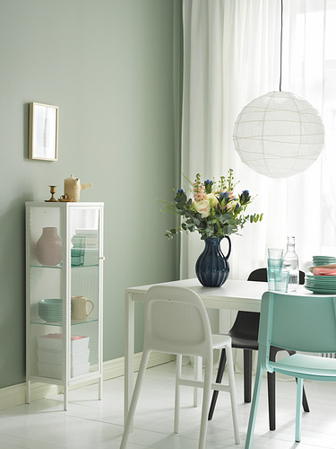 Comedor moderno con mesa blanca, sillas y armario BAGGEBO. Paredes verdes, centro de mesa floral y luz colgante.