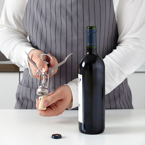 La persona usa una herramienta de sacacorchos para abrir la botella de vino, con palancas para facilitar el descorche.