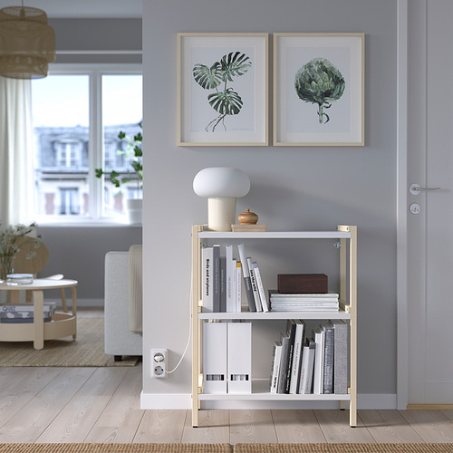 Salón moderno con estantería blanca EKENABBEN, estampados tropicales, libros, lámpara, sofá blanco, gran ventanal.