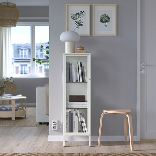 Vitrina de cristal blanco con libros, decoración, taburete de madera clara, estampados de hojas arriba, junto a la puerta y el sofá.