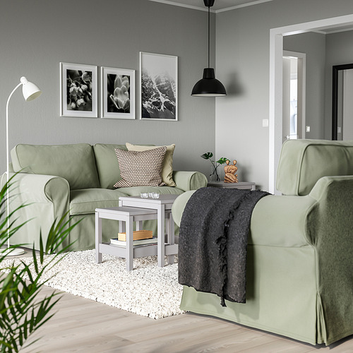 Acogedora sala de estar con sofás EKTORP de color verde claro, obras de arte en blanco y negro y una lámpara colgante negra, creando un espacio moderno pero acogedor.