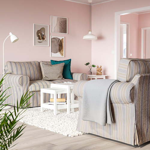 Una acogedora sala de estar, un sofá EKTORP a rayas grises y blancas con una pequeña mesa auxiliar, planta y lámparas en una habitación de paredes rosas.