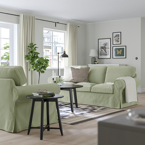 Sala de estar moderna con sofá EKTORP verde claro, mesas auxiliares negras, velas y arte de pared.