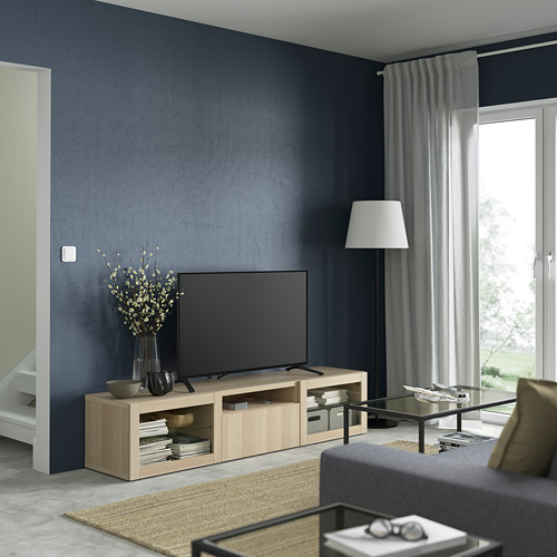 Sala de estar moderna con banco de televisión BESTÅ, sofá gris, mesa de centro con libros, alfombra ligera junto a la ventana.
