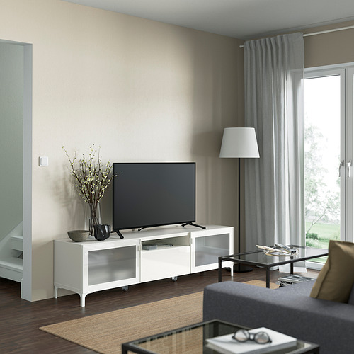 Sala de estar con mueble de tv NANNARP blanco, tv negra, lámpara de pie, cortinas grises, sofá gris y mesa de centro de vidrio.
