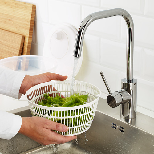 Persona lavando lechuga en colador blanco debajo de un grifo cromado moderno en el fregadero de la cocina.