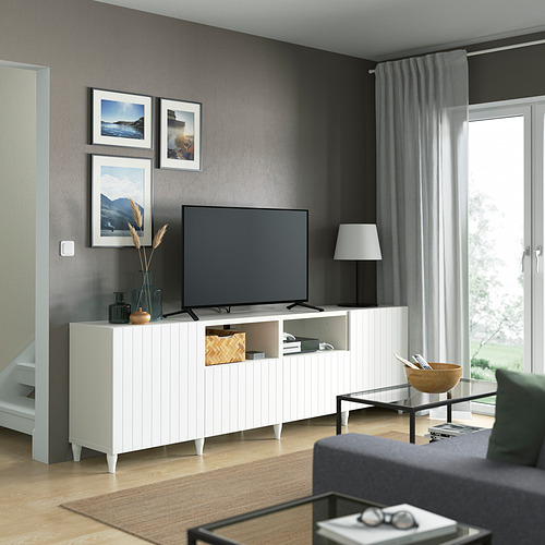 Salón moderno con banco de tv BESTÅ, paredes grises, cortinas, TV de pantalla plana, fotos, lámpara, mesa de centro, cuenco, alfombra, sofá verde.