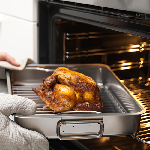 Una persona coloca un pollo asado en una fuente para asar de acero inoxidable con una parrilla en un horno.