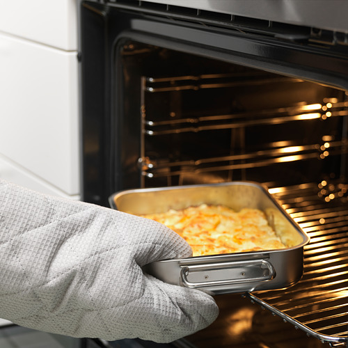 Sosteniendo con la mano un plato de metal con alimentos cocidos, colocándolo en el horno, demostrando la característica segura para el horno.
