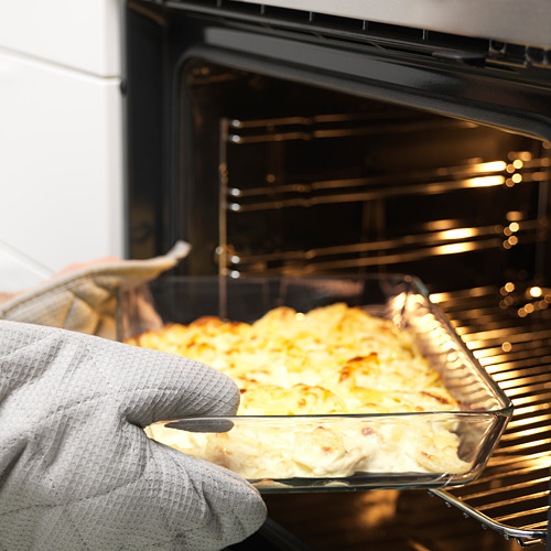 Persona con un guante de cocina que sostiene un plato de vidrio con comida horneada, sacándolo del horno.