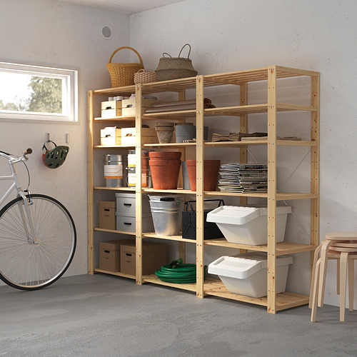 Un sistema de almacenamiento HEJNE hecho de madera de color claro con múltiples estantes que contienen varios artículos. Es más grande que la bicicleta y el taburete colocados cerca.