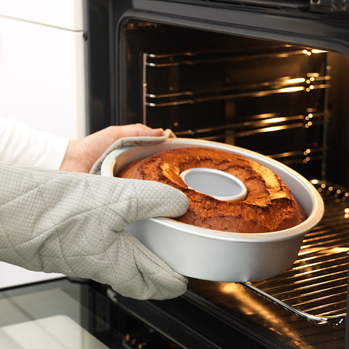 Una persona con guantes de horno retira con cuidado un bizcocho de color marrón dorado de un horno con un molde para hornear con una base extraíble.