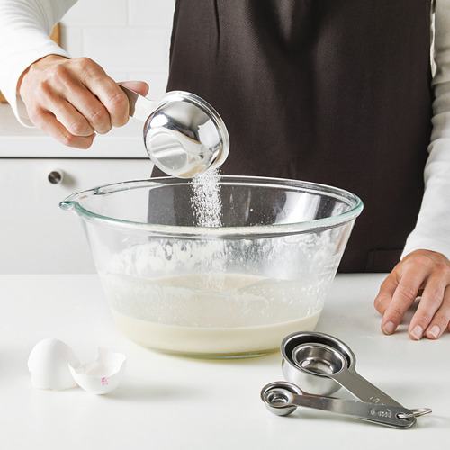 Una persona agrega ingredientes a un tazón para mezclar usando tazas medidoras. Las tazas se colocan sobre un mostrador, listas para mediciones precisas.