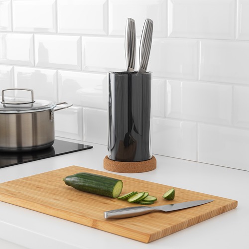 Bloque de cuchillos de ikea negro con cuchillos junto a tabla de cortar de bambú y pepino en rodajas.