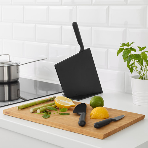 Cuchillos JÄMFÖRA negros sobre tabla de madera con frutas/verduras en rodajas; uno en bloque.