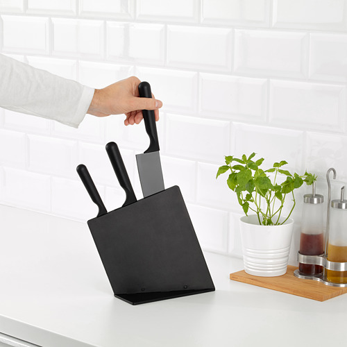Persona agarrando un cuchillo de un bloque negro en la encimera de la cocina, junto a la planta y los condimentos.