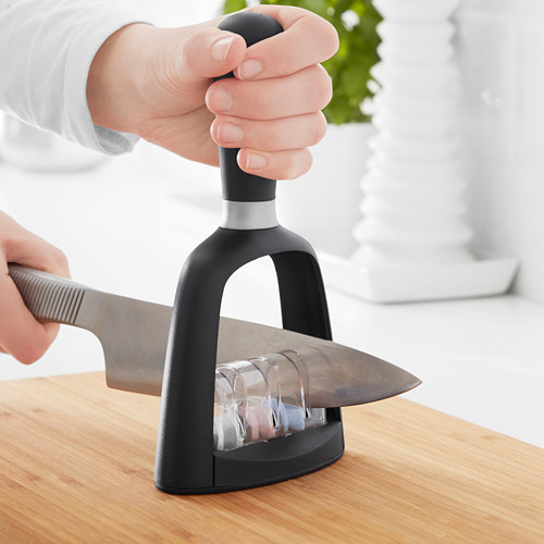 Persona afilando cuchillo con afilador eléctrico sobre mesa de madera.