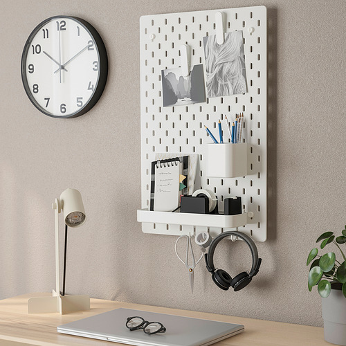 Organizador de pared con reloj, lámpara, artículos de escritorio y plantas. Expositores de tableros perforados SKÅDIS Accesorios de oficina y decoración cuidadosamente dispuestos.