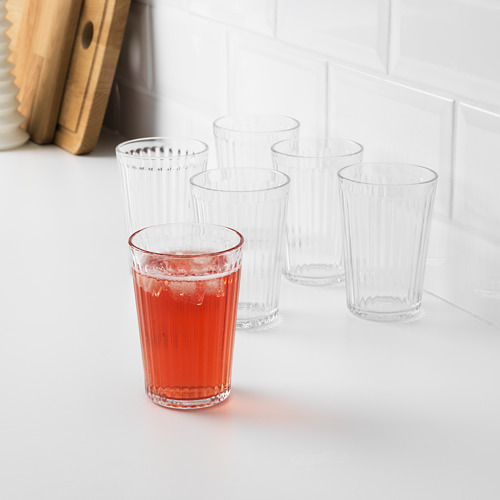 Seis vasos transparentes con crestas verticales, uno lleno de líquido rojo, sobre una encimera blanca, perfectos para servir bebidas.