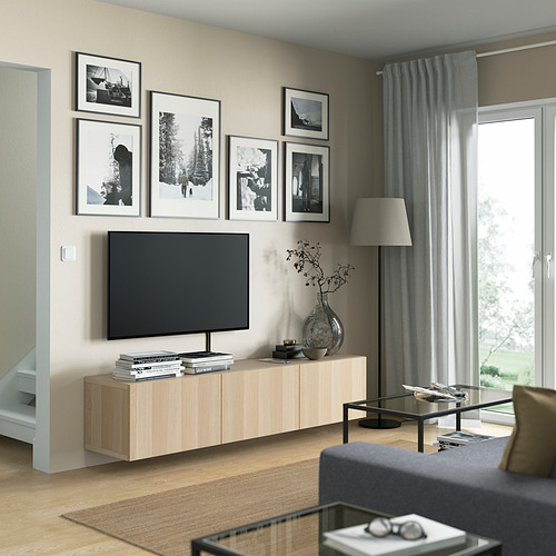 Sala de estar moderna con banco de televisión BESTÅ en roble claro, con estantes de almacenamiento, arte encima y un jarrón de plata a un lado.