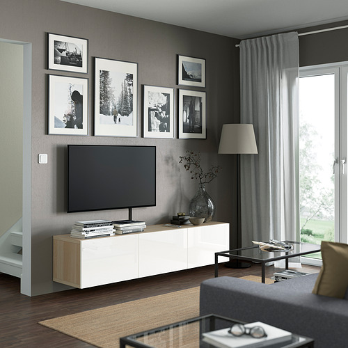 Sala de estar moderna con un gran televisor montado sobre un banco de televisión BESTÅ blanco. El banco tiene marcos negros, una mesa de centro de vidrio y un sofá negro.