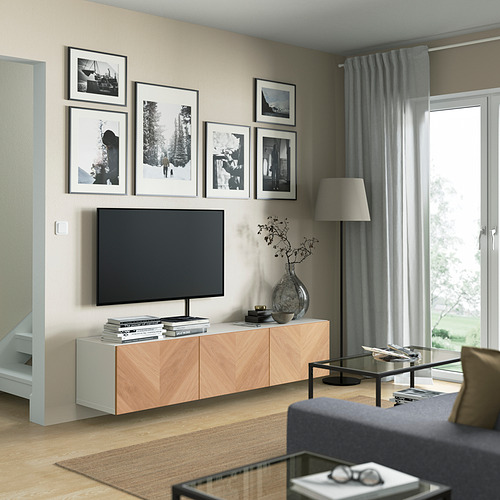 Salón moderno con banco de tv BESTÅ, TV de pantalla plana, fotos, estantes ajustables, jarrón, mesa de cristal, sofá gris, grandes ventanales.