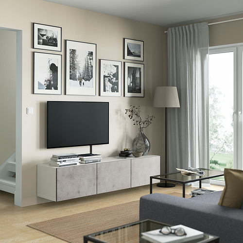 Sala de estar moderna con banco de tv BESTÅ, tv montada, libros, jarrón, fotos, lámpara y sofá gris.