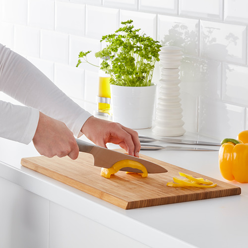 Persona cortando pimiento amarillo en una tabla de cortar de madera con un cuchillo.