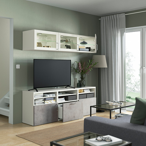Sala de estar moderna con mueble de TV BESTÅ, estantes ajustables y armarios de pared. TV de pantalla plana, decoración y lámpara en las inmediaciones. Mesa de centro de cristal en el frente.