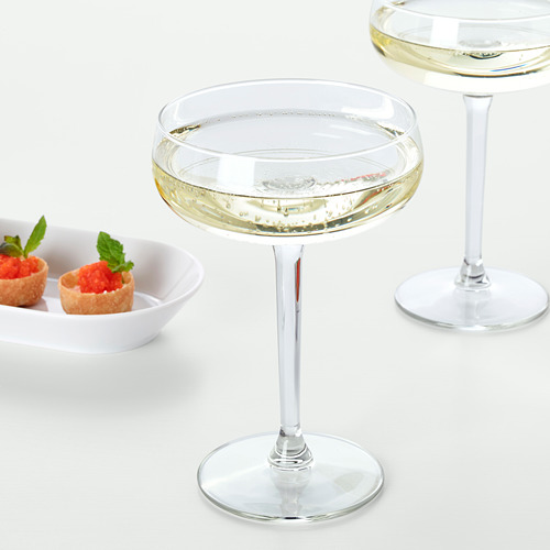 Dos copas de vino rellenas de vino espumoso, acompañadas de un pequeño plato de tazas de postre adornadas con hojas de menta.