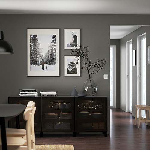 Modern dining room with black BESTÅ sideboard, plates, branches, books, nature photos, pendant light, and light chairs around black table.