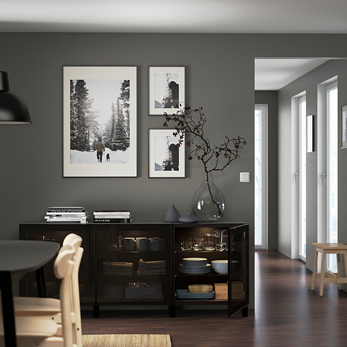 Modern living room featuring adjustable, wall-mounted BESTÅ storage with glass doors showcasing plates and a decorative vase, alongside framed art.