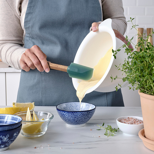 Persona que vierte líquido de un recipiente con una espátula. Los tazones con los ingredientes están en la mesa.