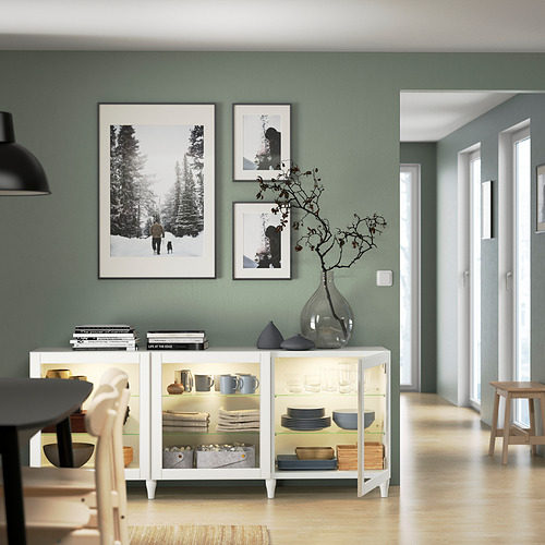 Comedor moderno con aparador BESTÅ, vajilla, decoración y libros. Las obras de arte cuelgan por encima.