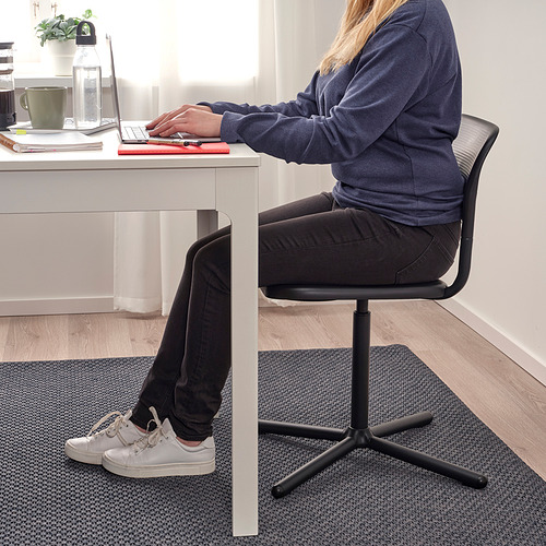 Persona sentada en un escritorio blanco sobre una silla giratoria SMÄLLEN con una alfombra gris.