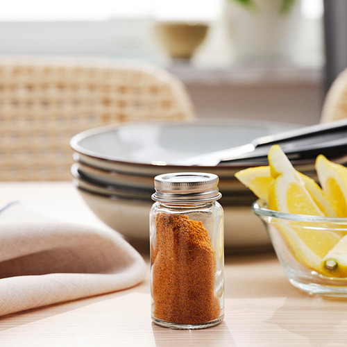 Frasco de vidrio pequeño con especias, con tapa, en la mesa junto a rodajas de limón, servilletas y platos.