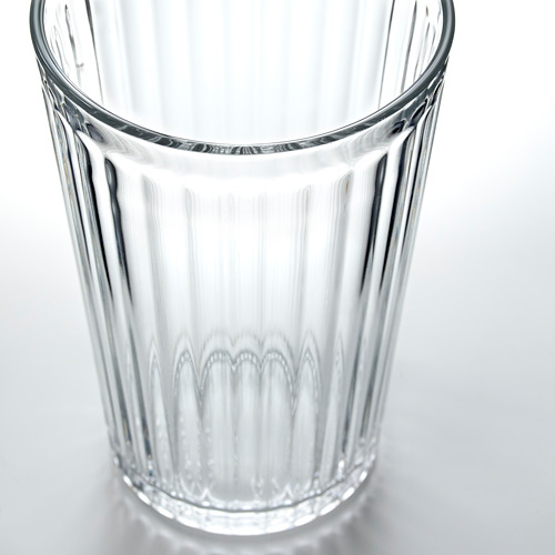 Vaso de vidrio con crestas verticales, claro y transparente, que descansa sobre una superficie blanca.