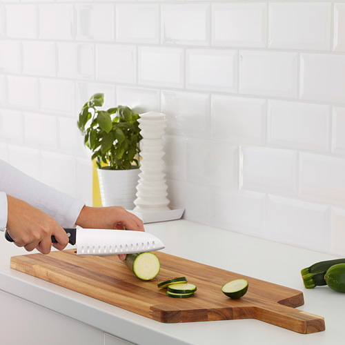 Una persona corta el pepino en rodajas en una tabla de cortar de madera sobre una encimera de cocina blanca.