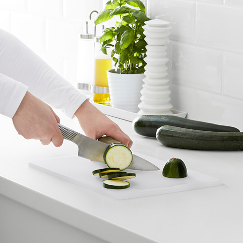 Persona cortando calabacín en una pizarra blanca con cuchillo en la cocina.