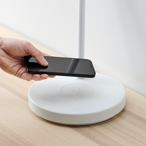 Persona colocando el teléfono inteligente en una plataforma de carga inalámbrica blanca sobre un escritorio de madera.