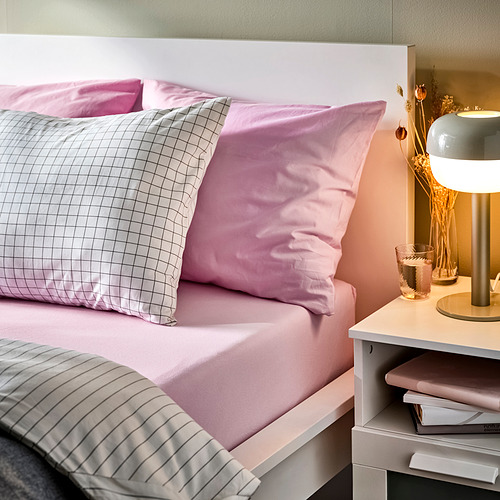 Cama con sábanas de algodón rosa DVALA , cojines a juego y una mesilla de noche elegante con lámpara y libros.