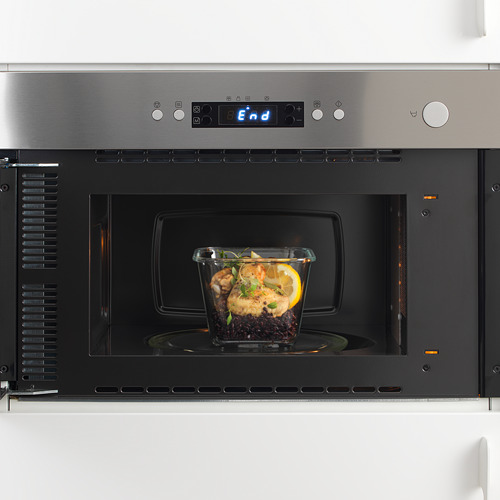 Microondas empotrado de acero inoxidable con recipiente de vidrio en su interior, mostrando su función como calentador de alimentos.