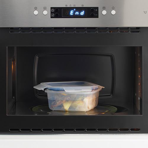 Un microondas con un recipiente de plástico transparente que contiene las sobras en su interior, lo que demuestra el almacenamiento y el recalentamiento de alimentos.