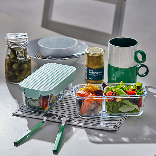 Mostrador de cocina con fiambrera, pepinillos, taza y utensilios.