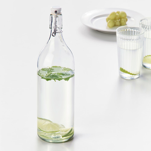 Botella de vidrio con rodajas de lima y menta, tapón sellado.